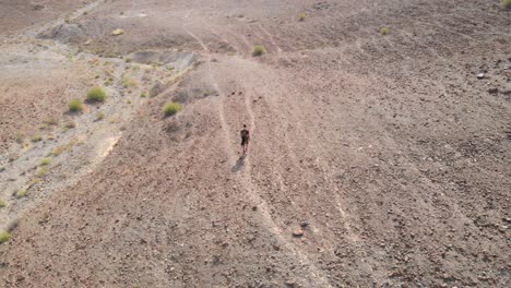 aerial circular shot from drone of an young male walking in a rocky desert valleys in hatta, united arab emirates