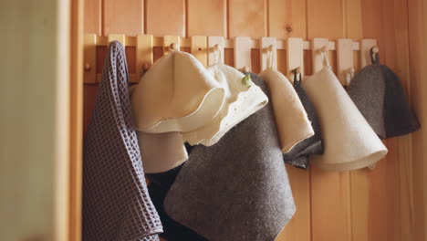wooden sauna corner with hook rail displaying hanging waffle towels and felt hats, warm natural light accentuating pine panel texture and soft shadows