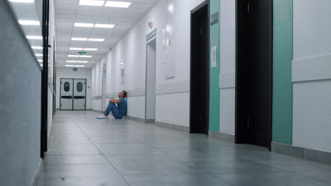 weary surgeon sitting floor modern clinic. doctor resting on hospital corridor.