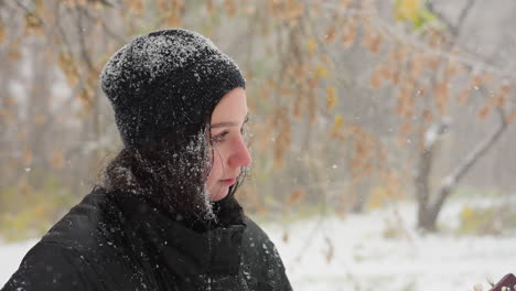 close-up of young woman in black beanie and winter coat covered with fresh snowflakes feeling focus on guitar, with serene snowy trees blurred in background