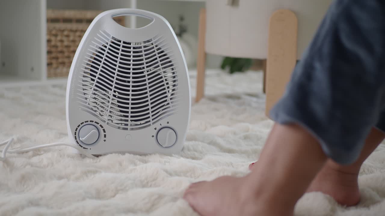 Bare Feet Warming Up with a Portable Electric Fan Heater