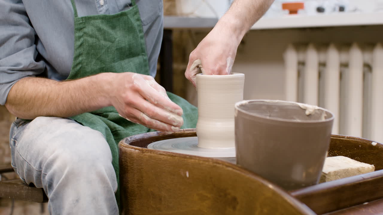 작업장에서 물레에 세라믹 조각을 모델링하는 점원의 손을 가까이서 볼 수 있습니다.