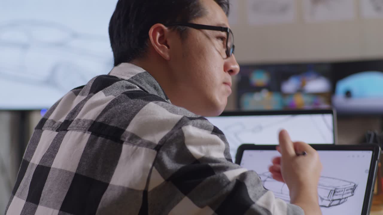 Close Up Side View Of Asian Male Thinking About New Car Concept Then Raising Index Finger While Drawing On Tablet In The Studio With Tv And Computers Display 3D Electric Car Model