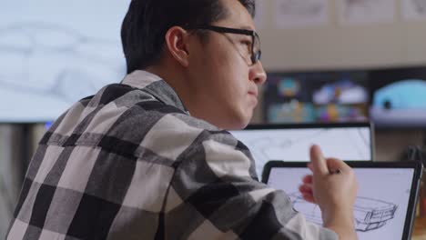 close up side view of asian male thinking about new car concept then raising index finger while drawing on tablet in the studio with tv and computers display 3d electric car model