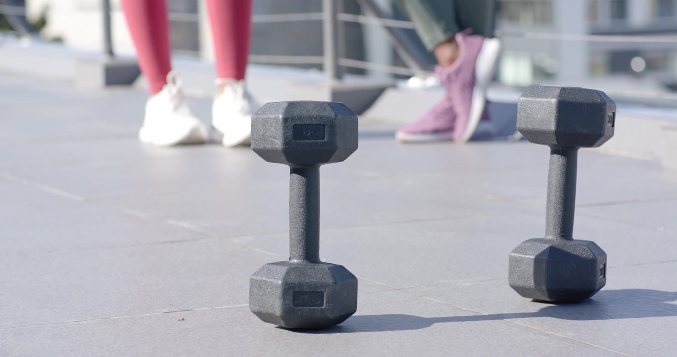 Spotting dumbbells, African American women stepping, placing feet and training in leggings on roof