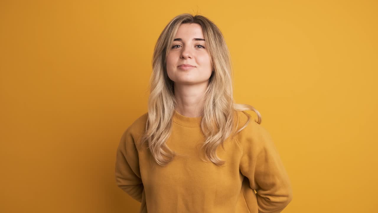 Happy young woman presenting gift box with ribbon on yellow background