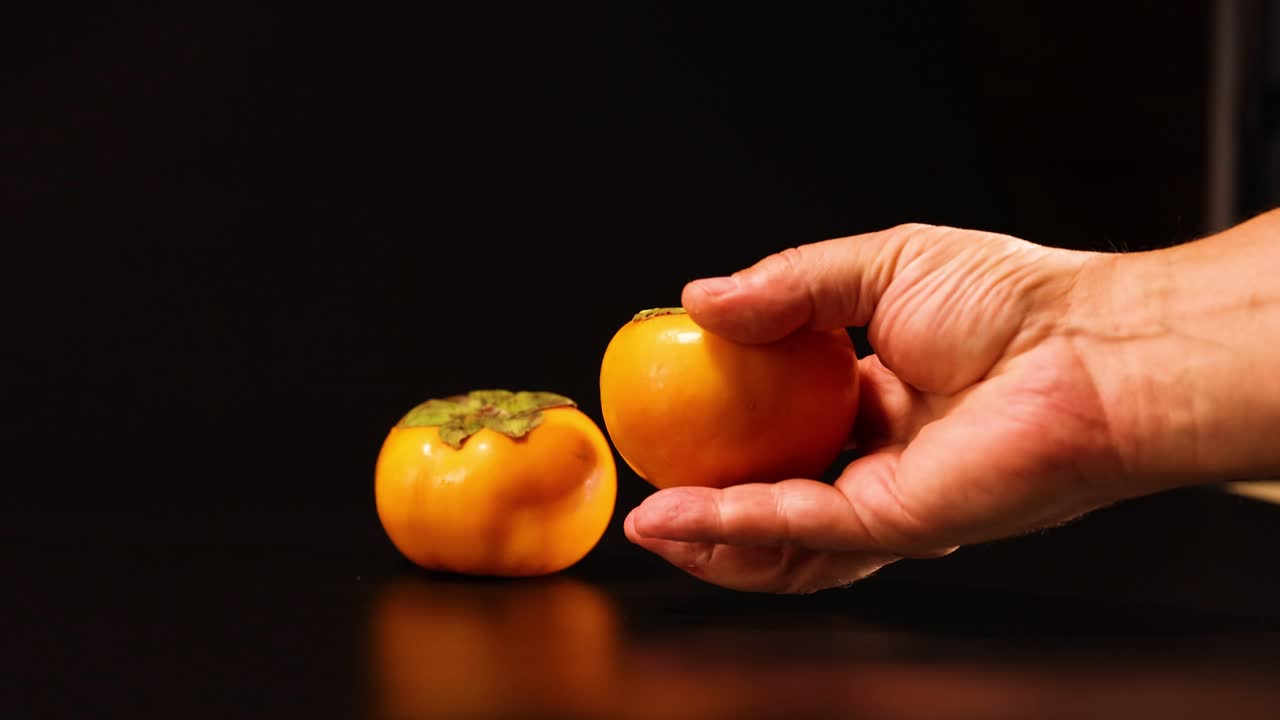 A hand reaches for a persimmon fruit