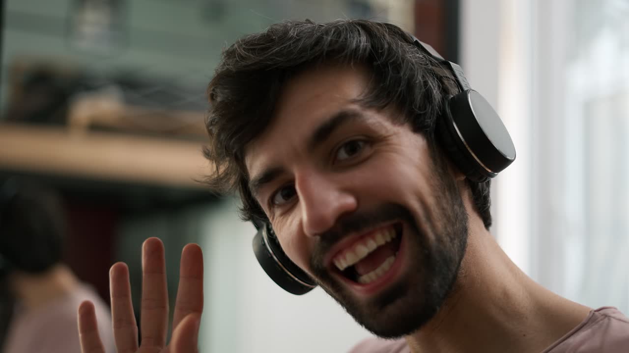 hombre joven mirando a la cámara en auriculares inalámbricos agitando a la cámara