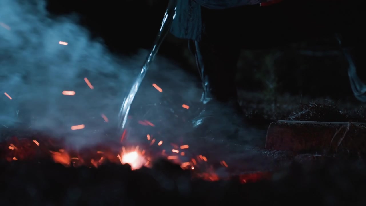 Due flussi di metallo fuso cadono in braci incandescenti, sprigionando scintille arancioni brillanti e fumo grigio-blu che si arriccia, mentre una vista ravvicinata dal basso evidenzia calore intenso, fuoco e texture industriale.