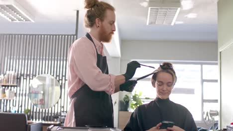 caucasian male hairdresser highlighting female client's hair with brush at salon, in slow motion