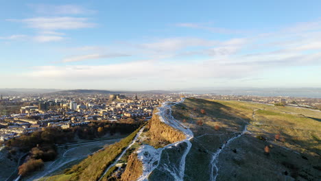 una foto aérea del asiento arthur de edimburgo cubierto de nieve en un hermoso día de invierno