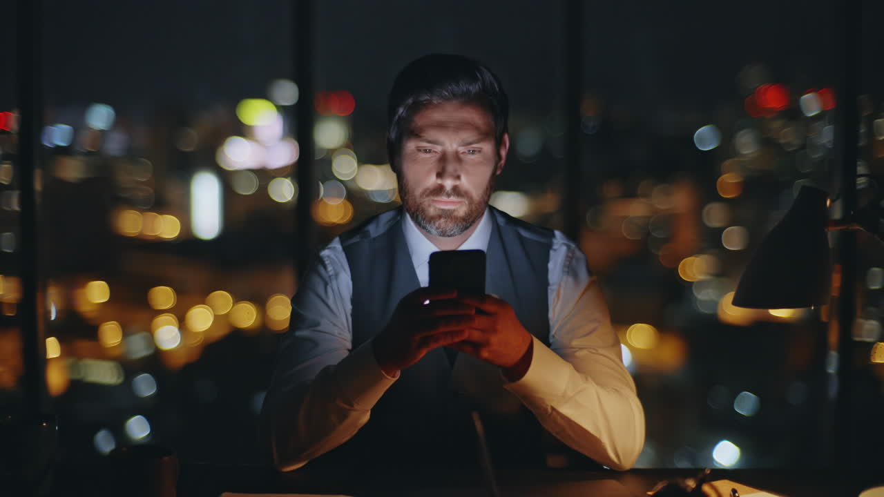 Corporate boss messaging mobile phone at evening city view. Late man work office