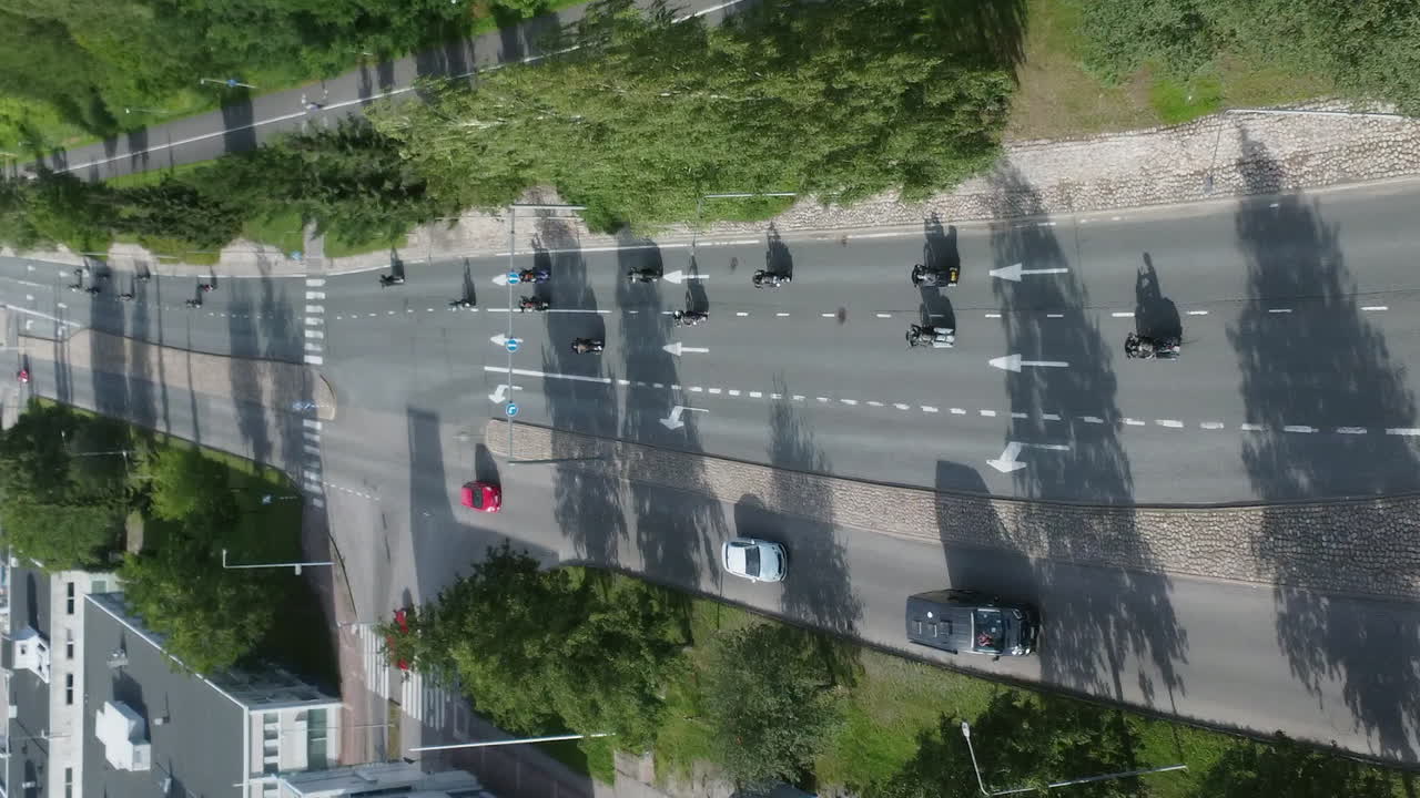 Vertical format aerial follows motorcyclists riding in group on street