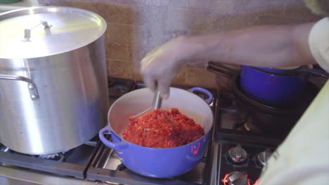 man mashing raspberries in blue pot for jam