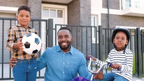 Portrait-of-joyful-African-American-father-smiling-to-camera-with-small-kids-at-street-in-outskirt