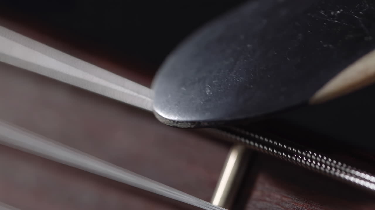 Vista Macro de Palheta de Guitarra em Corda de Aço Próximo ao Rastilho da Ponte, Luthier Afinando e Músico Dedilhando