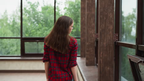 lady strolls arching neck back by windows. woman finds solace within expansive studio adorned floor-to-ceiling windows. comfort of sanctuary