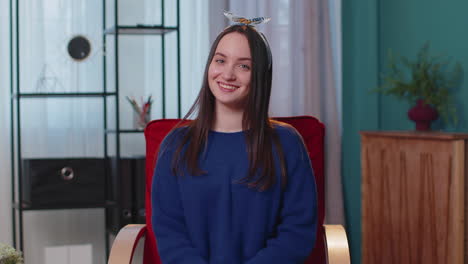 Portrait-of-happy-one-beautiful-teenager-student-girl-smiling,-looking-at-camera-at-home-on-chair