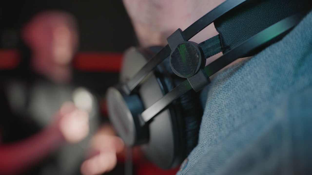 헤드폰을 착용한 남자의 목의 클로즈업, 부드럽게 흐릿한 배경에 파란 셔츠를 입고 미소 짓고, 방음 스튜디오에서 편안한 순간을 포착합니다.