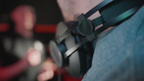 un primer plano del cuello de un hombre con auriculares, sonriendo en una camisa azul contra un fondo suavemente borroso, capturando un momento relajado en un estudio a prueba de sonido