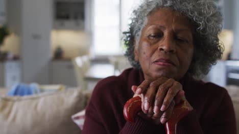 thoughtful senior african american woman holding walking stick sitting on the couch at home