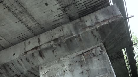 concrete support beams holding up road way, view from underneath weathered grey black bridge