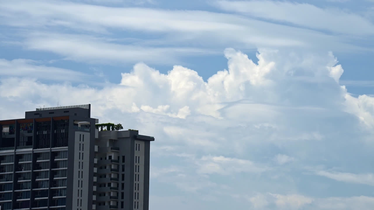 Timelapse diurno che cattura il movimento delle nuvole attraverso un cielo blu brillante, sullo sfondo dell'architettura di un moderno edificio residenziale a molti piani.