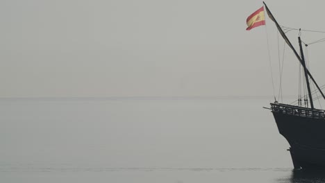 Ferdinand-Magellan-Nao-Victoria-carrack-boat-replica-with-spanish-flag-sails-in-the-mediterranean-at-sunrise-in-calm-sea-exiting-the-frame-in-slow-motion-60fps