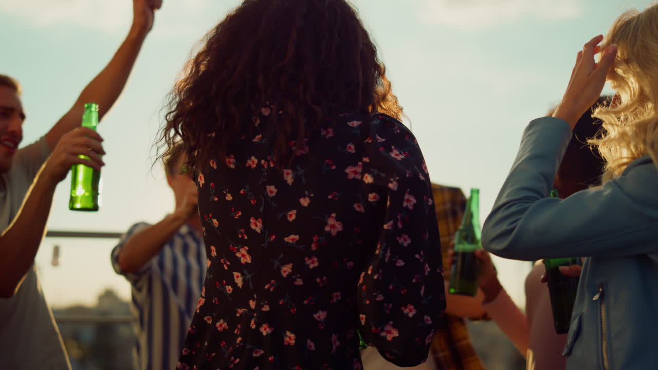 Multiethnic friends toasting with beer at sunset party. Smiling friends dancing.