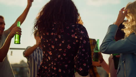 multiethnic friends toasting with beer at sunset party. smiling friends dancing.