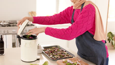 Mid-section-of-biracial-woman-putting-waste-into-bin-in-kitchen-at-home-with-copy-space,-slow-motion