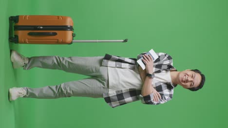 full body of asian male traveler with luggage and passport crossing arms and smiling to camera while standing in the green screen background studio