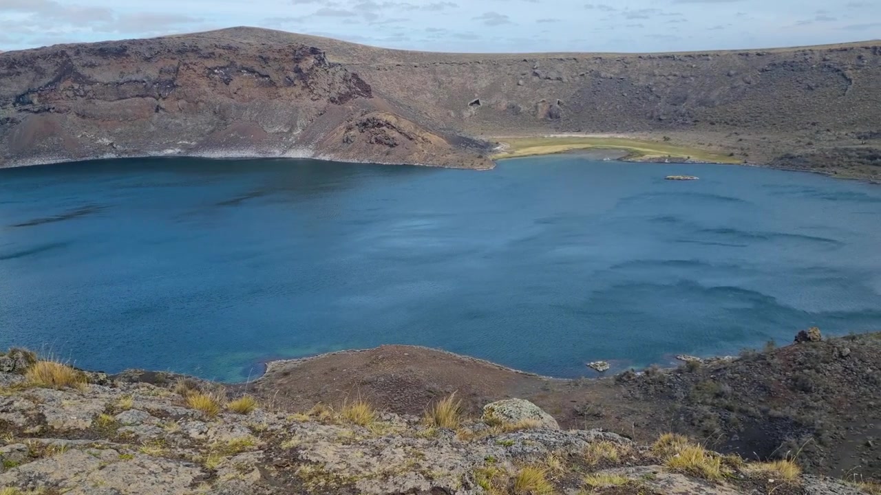El viento barre las aguas azul profundo de la Laguna Azul, un lago de cráter volcánico en el campo volcánico Pali Aike, cerca de Río Gallegos, Patagonia, Argentina. Escenario espectacular para viajes por carretera y turismo de naturaleza.
