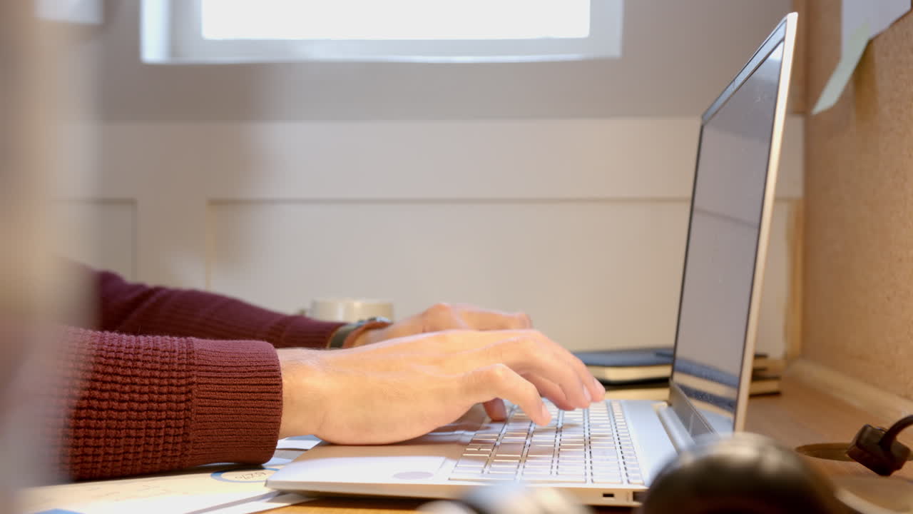 Typing on laptop, man working from home at desk with coffee mug, copy space