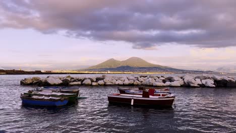 Pequeños-Barcos-Atracados-En-Nápoles-Con-Una-Vista-Panorámica-Del-Monte-Vesubio-Durante-La-Puesta-De-Sol.