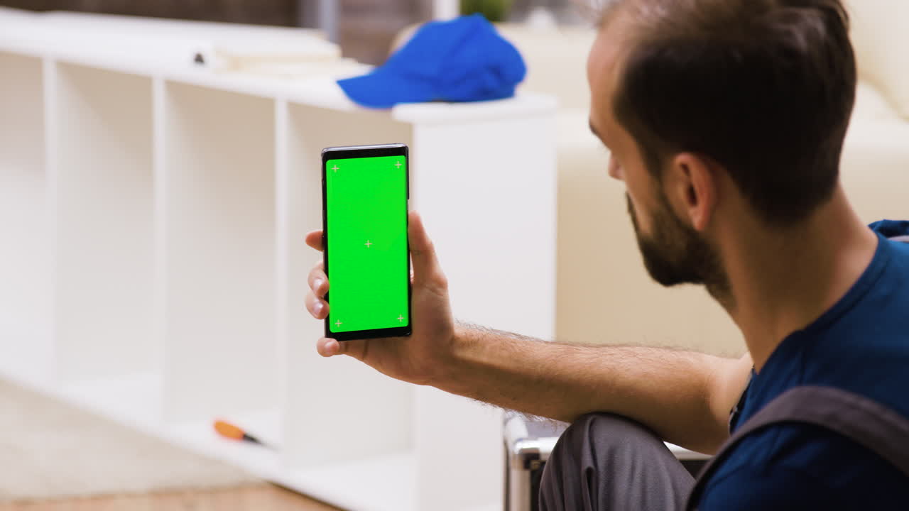 Man Holding Phone with Green Screen in Front of Shelves