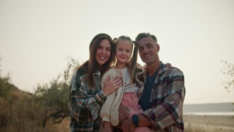 retrato de una familia feliz, una pequeña chica rubia se sienta en los brazos de su padre, un hombre moreno con un poco de cabello gris en una camisa a cuadros marrones, a su lado está su madre, una chica morena en una camiseta a cuadros verdes. familia en una caminata y en un picnic fuera de la ciudad