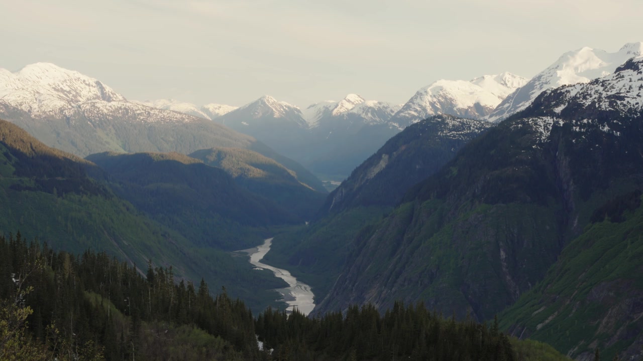 Brefylt elv som renner gjennom en frodig grønn dal med snødekte fjell i Britisk Columbia, Canada.