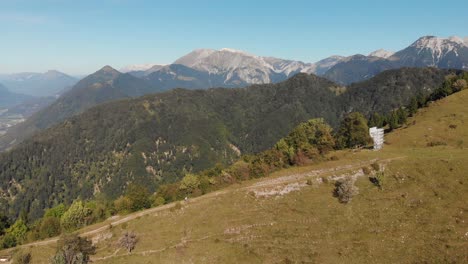 aerial shot of mountain biker climbing gravel road uphill on grassy slope, mountains and valley in background, summer sunny day with clear sky