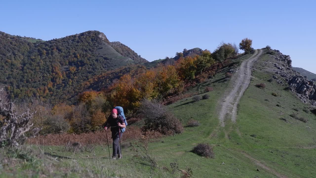 un excursionista caucásico camina hacia una cámara de bajo ángulo en las montañas de otoño