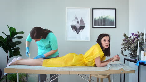 two girls in a beauty salon master in a bathrobe and gloves doing the procedure to remove hair on the legs with a sugar mixture