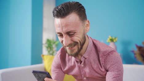 Happy-young-man-using-his-smart-mobile-phone-at-home.