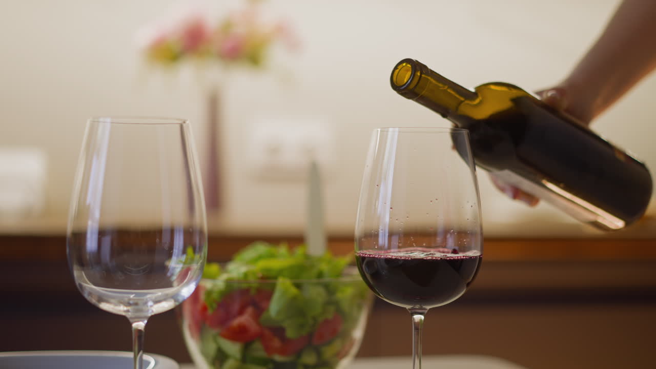 Woman fills wineglass with red wine serving romantic supper