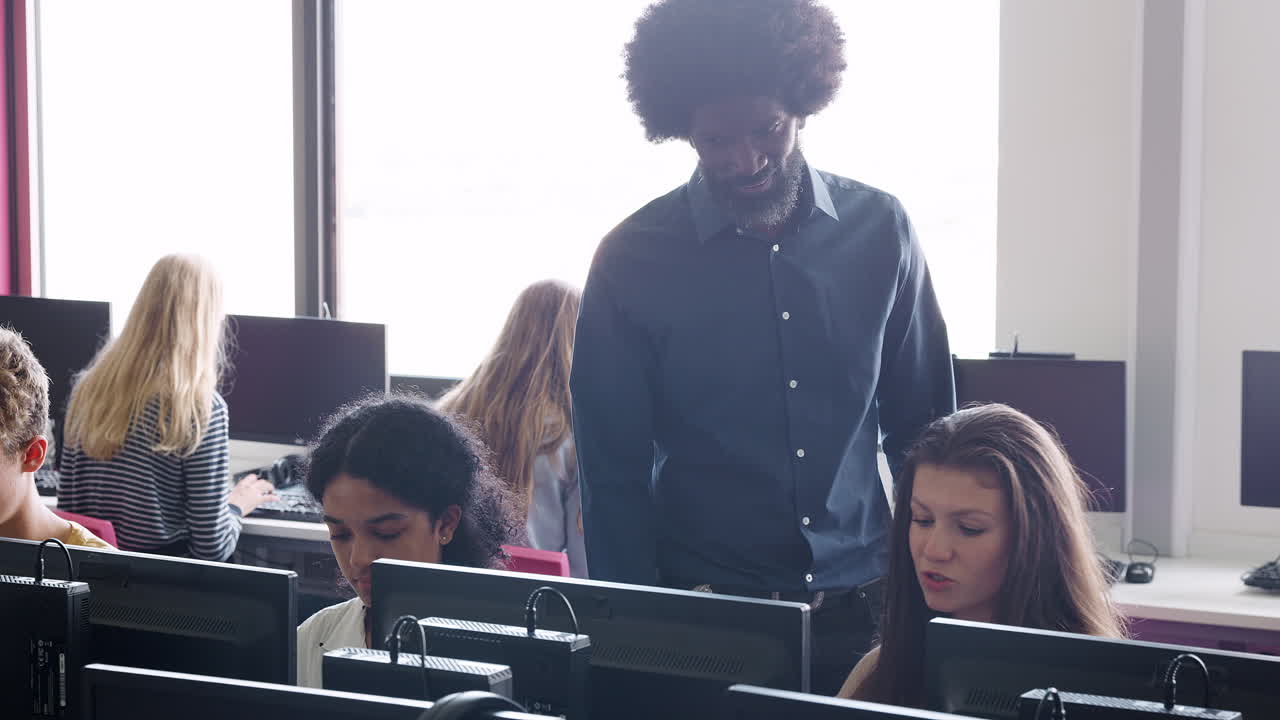 Male Teacher Helping Teenage Female High School Student Working In Computer Class