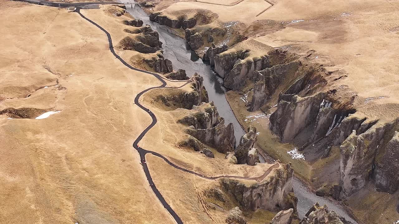 Aerial view of the winding Fjaðrárgljúfur Canyon with rugged cliffs, a flowing river, and golden landscapes near Kirkjubæjarklaustur, Iceland.