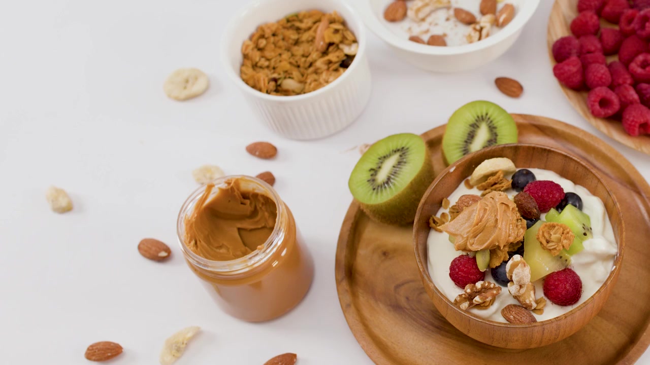 Top-down view of a hand gesturing over a yogurt bowl with berries and nuts.