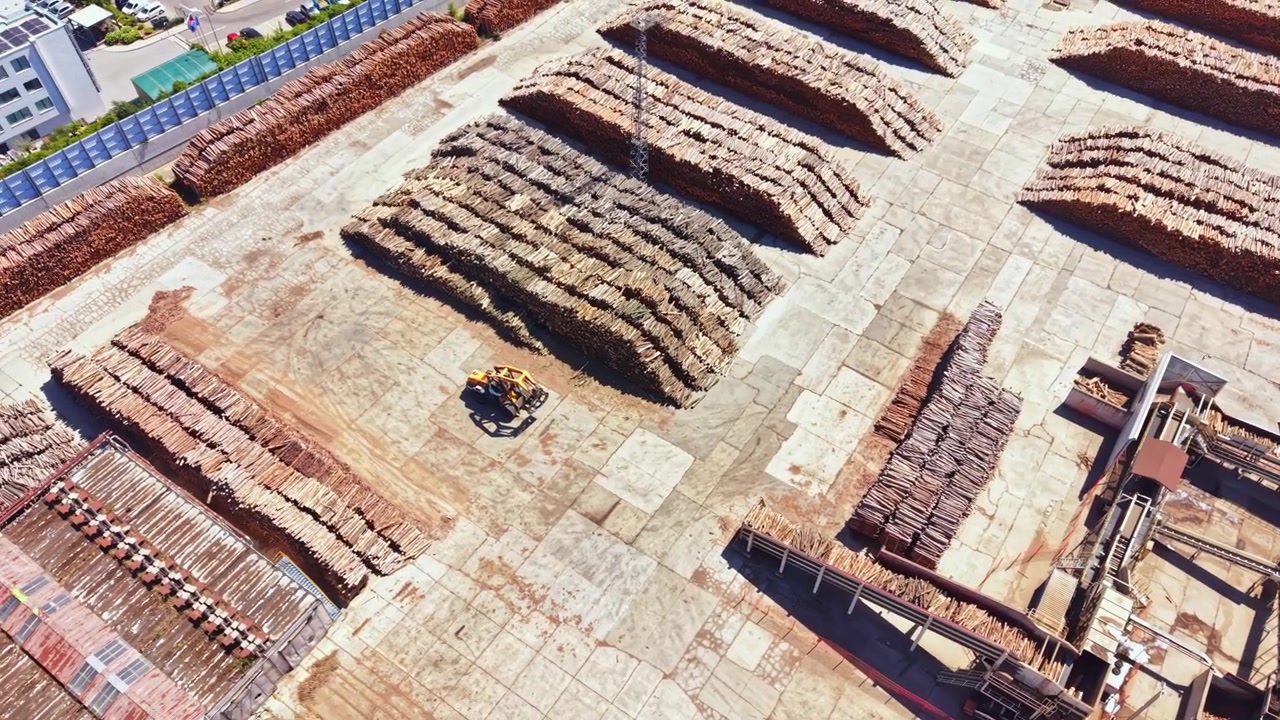 Wood processing area with stacked logs and machinery in operation during day