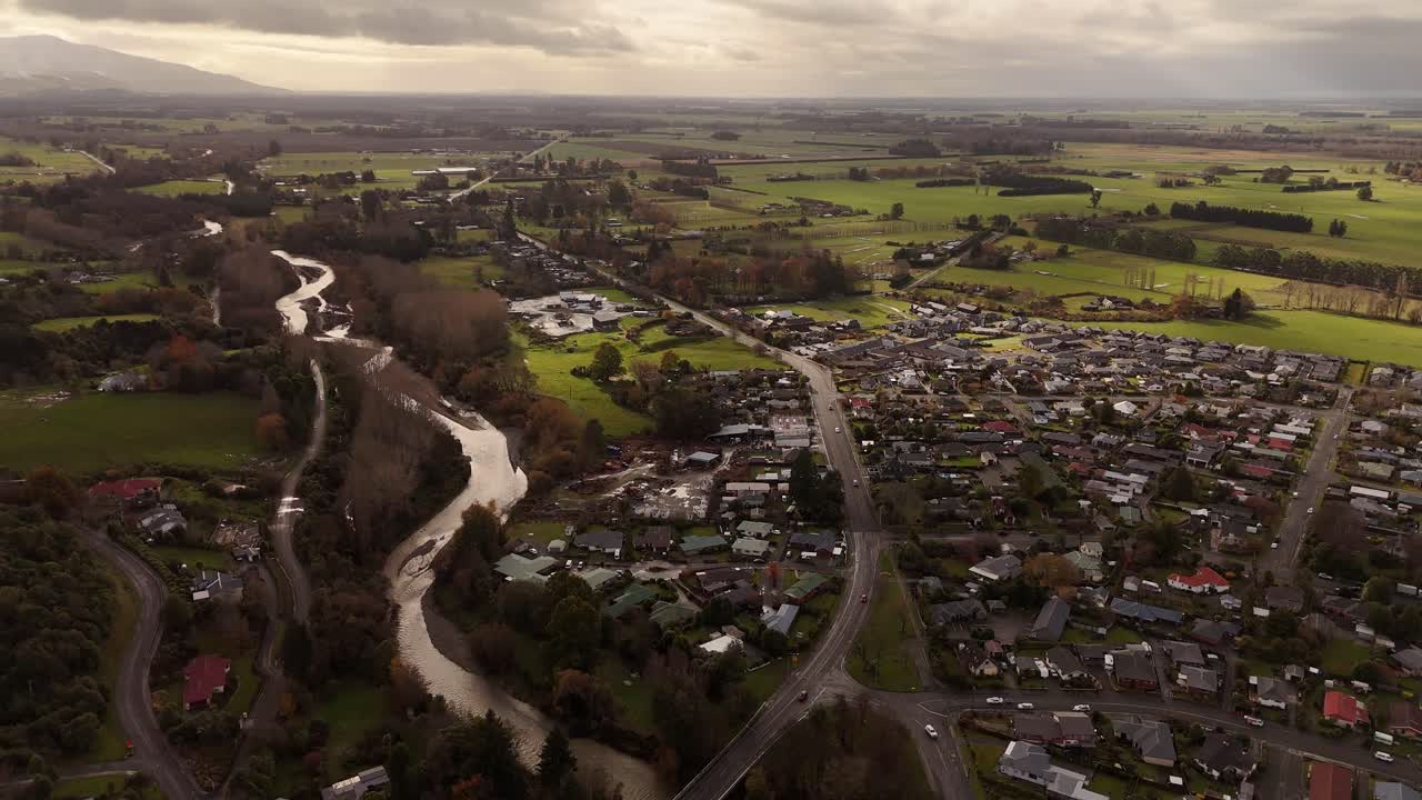 A beautiful 4K aerial view showcasing both Geraldine town and the meandering Te Moana River in New Zealand's scenic Canterbury region. Snowy mountains are visible in the distance