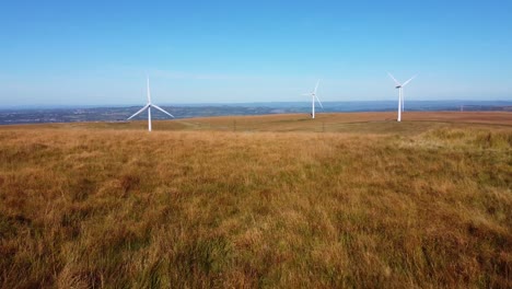 low flying drone aerial view of wind turbine farm with moorland grass blowing with beautiful blue sky background. renewable, sustainable, eco-friendly energy concept footage 4k