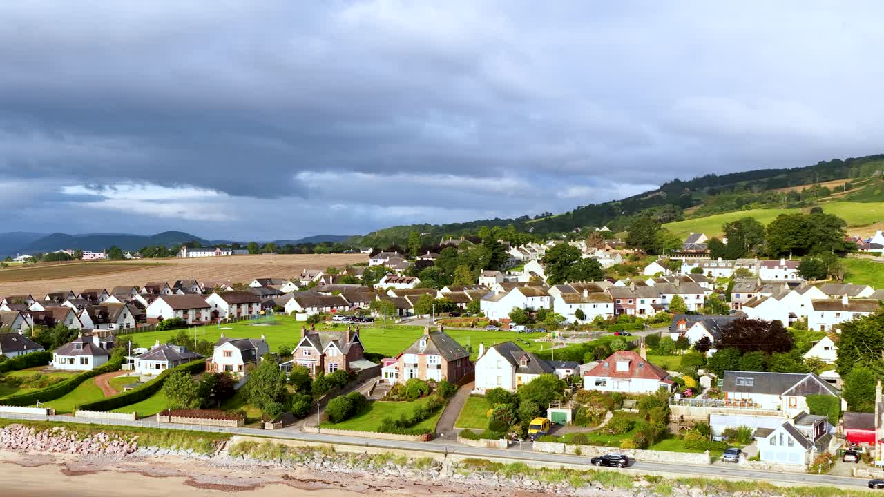 Droneoptagelser over landsbyen Rosemarkie viser huse ved stranden, grønne bakker og en dramatisk himmel